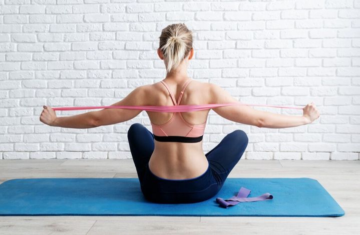 Rear view of blond woman training her back muscles using resistance band