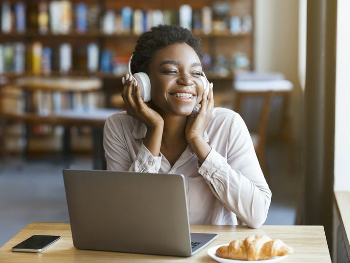 Black woman listening to music with headset, laptop in cafe