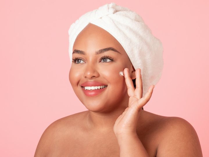 Skin care concept. Closeup portrait of black plus size lady applying moisturizing cream on face