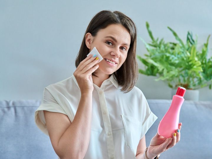 Young woman cleans her face with cotton pads, using cosmetic tonic