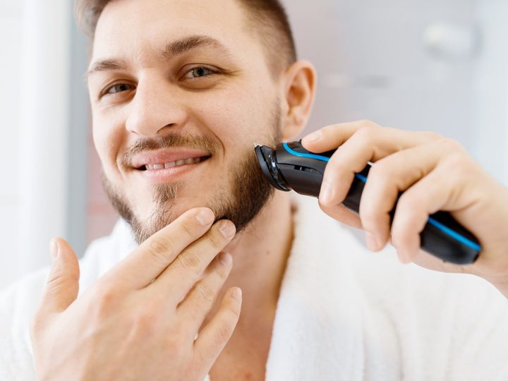 Man shaves his beard with an electric razor