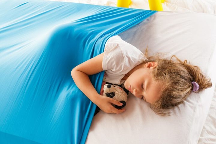 Cute blonde Caucasian girl sleeping on a mattress under a blue cozy blanket