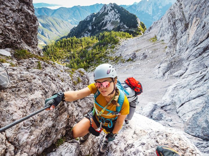 Smiling caucasian woman mountaineer with sunglasses on via ferrata trail in the Alps on a sunny