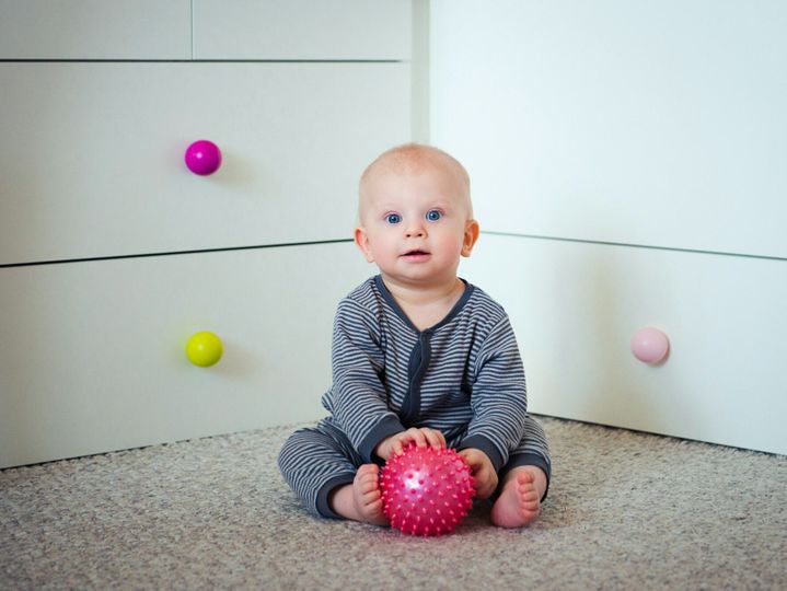 Cute 7-month baby with massage ball sitting on floor