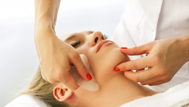 Beautician cosmetologist makes lifting modeling face massage with Gua Sha quartz scraper