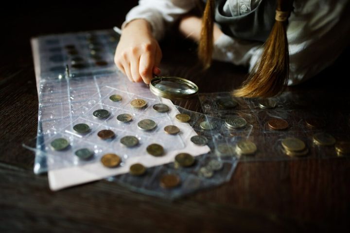 Cute cute european girl child in glasses with magnifying glass looks at coins