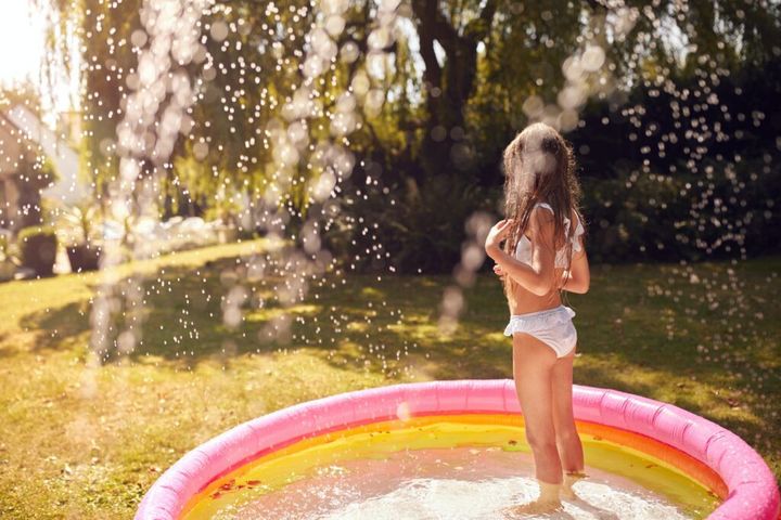 Girl Wearing Swimming Costume Having Fun In Summer Garden Playing In Water From Garden Sprinkler