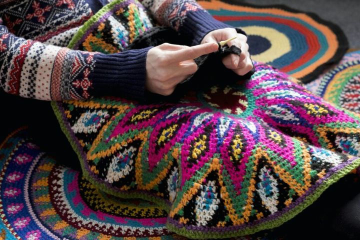 Mid section of woman sitting on floor crocheting, surrounded by crochet circles