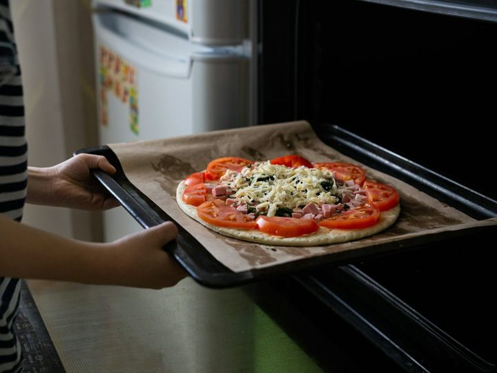 Home cooking, the child's hands hold a pizza pan in their hands, pizza baking in the oven