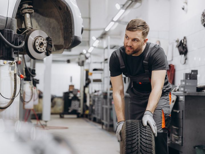 Happy Smiling Car mechanic working in garage and changing wheel alloy tire