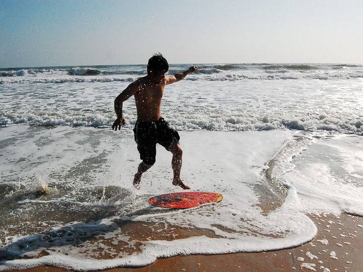 Young man jumping onto a red skimboard at the beach