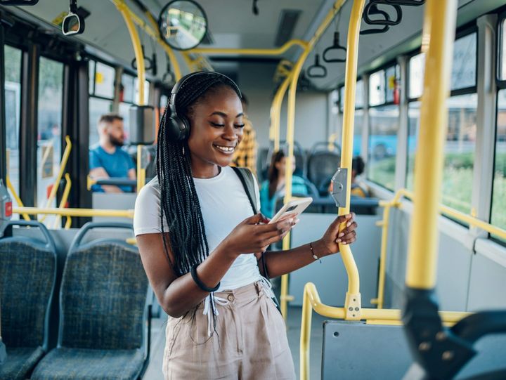 African american woman riding in a bus and using a smartphoneand headphones