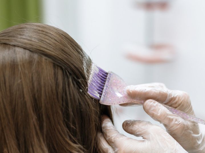 process of coloring the hair and painting over the gray hair of a young woman in a beauty salon