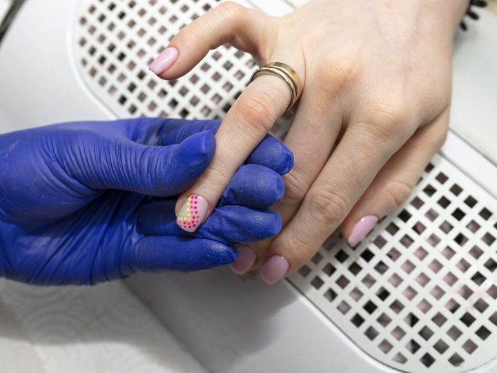 The manicurist paints her nails with pink hybrid varnish, and with a thin brush she paints pink dots