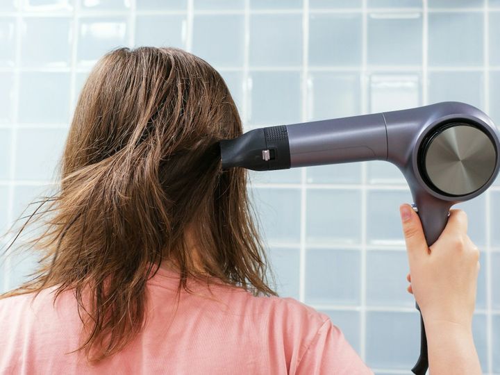 Young woman drying her hair with hairdryer in the bathroom close-up back view.