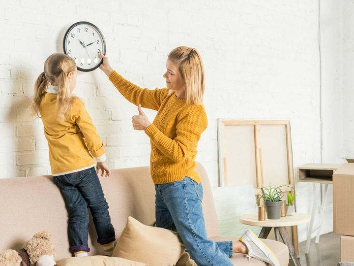 mother and daughter hanging clock on wall during relocation