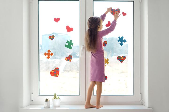 Girl decorates the window in the room with heart-shaped stickers and puzzles