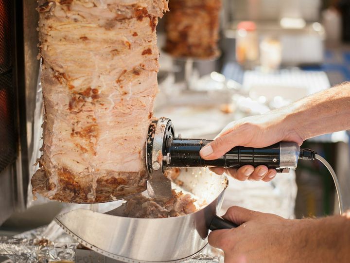 Hands of the Cook that with electric knife cut the doner kebab.