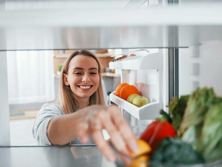 Happy woman taking vegetable from the fridge