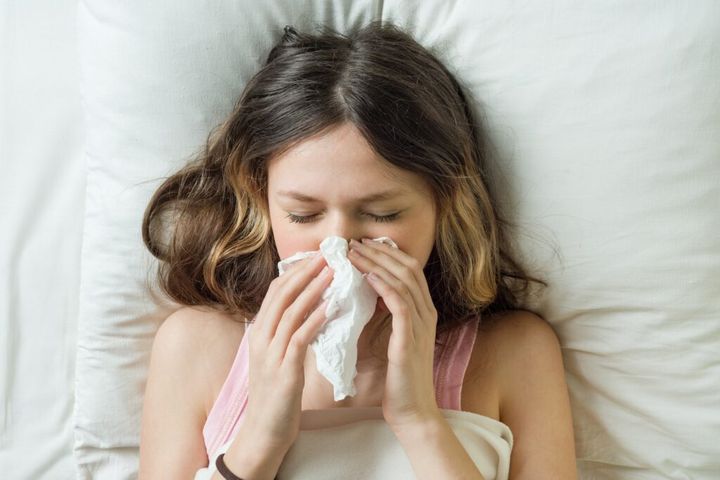 Cold flu season, runny nose. Sick girl on bed sneezing in handkerchief in bedroom