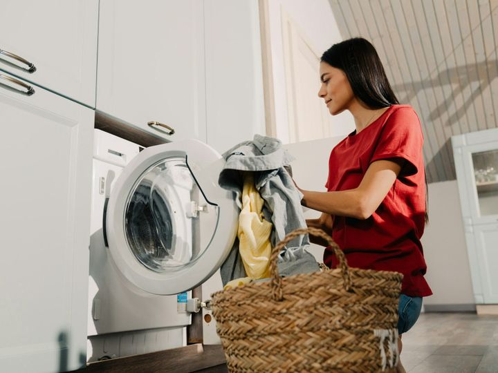 Young woman putting clothes at washing machine while doing laundry