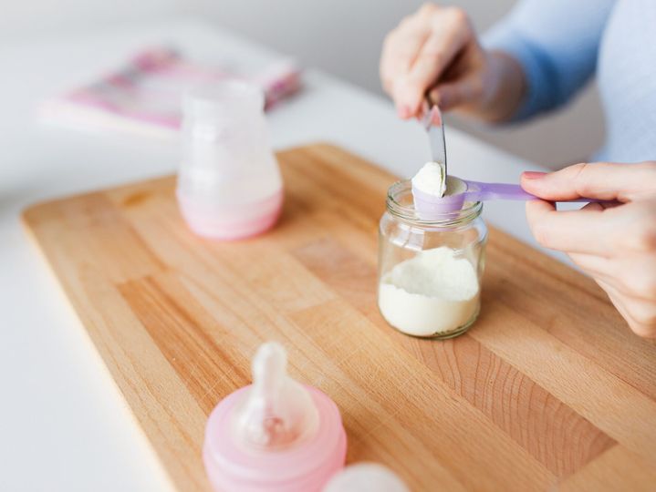 hands with jar and scoop making formula milk