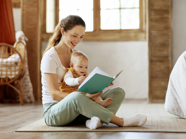 Smiling young mother read book with small baby at home