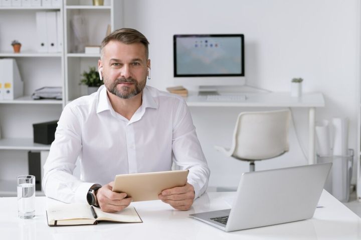 Confident entrepreneur with tablet and airpods looking through online data