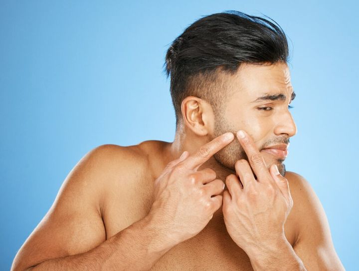 Health, skincare and man popping acne in face with blue background. Mens skin care, morning facial