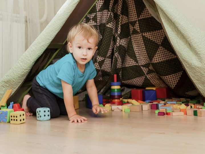 Little boy sitting on floor in kids room with toys.