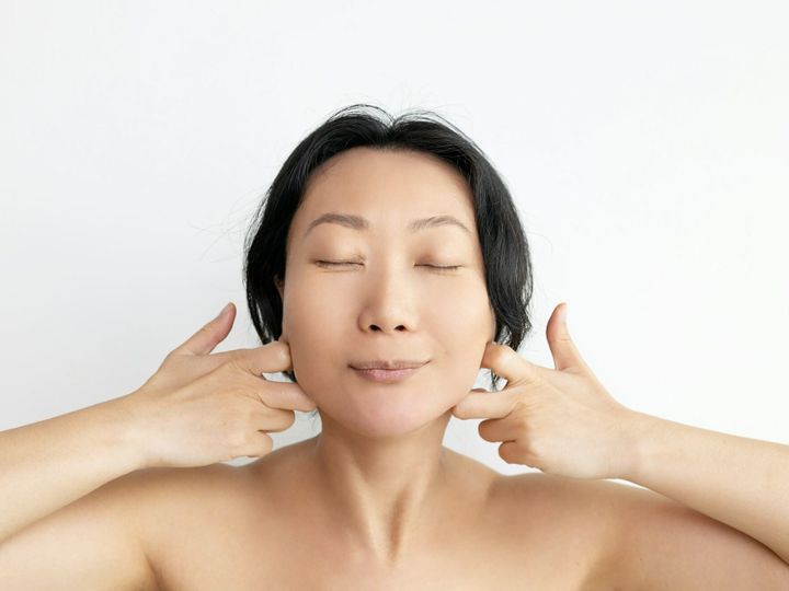 Young asian woman doing face building facial gymnastics self massage and rejuvenating exercises touc