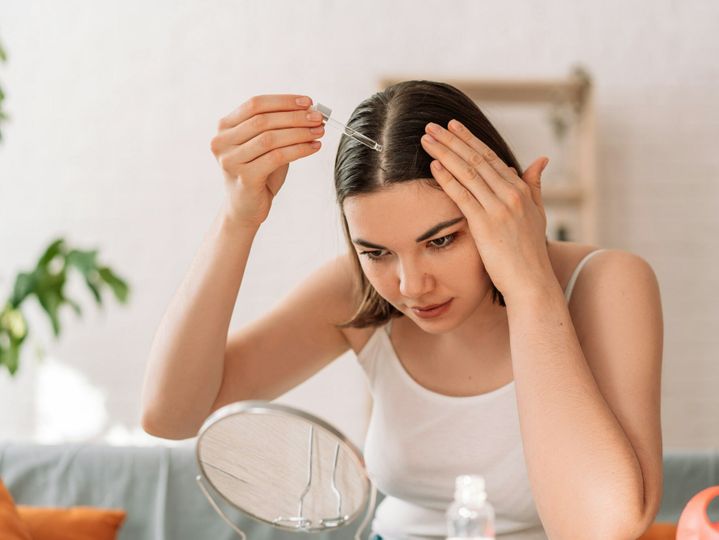 Lady sitting on the couch looks in the mirror and drips hair oil with a pipette on her hair