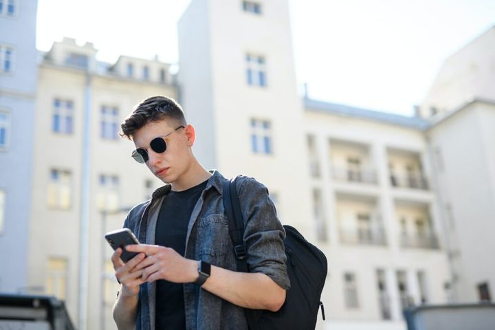 Portrait of young man standing outdoors in city, using smartphone