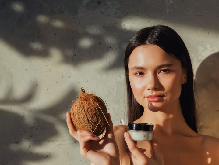 Face of woman holding coconut cream for face skin at textured wall backdrop
