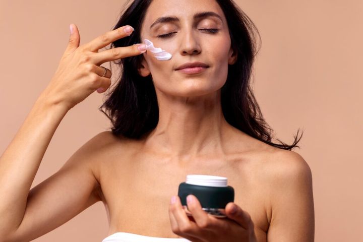 attractive young woman applying moisturizing cream to her face