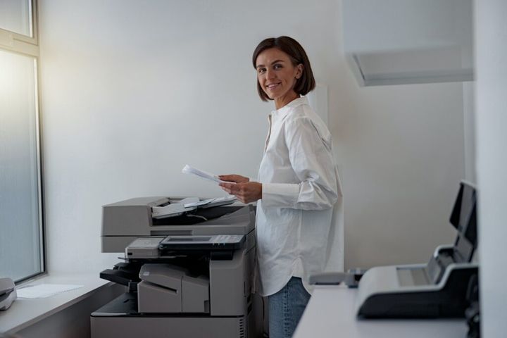Smiling woman worker scanning a document on photocopy machine In modern office
