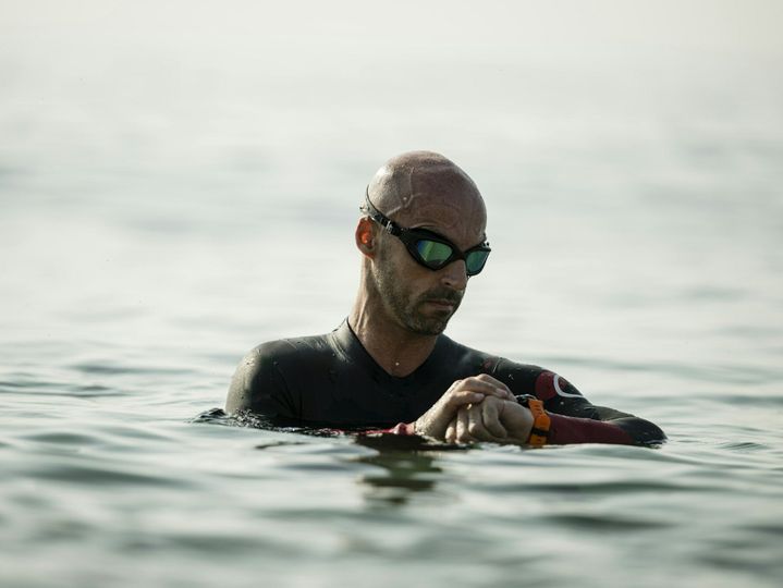 Confident man swimming in the ocean wearing glasses looking at his watch. Swimmer standing in the