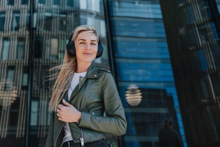 Confident blonde girl in headphones hair, leather jacket, white t-shirt smiling, enjoys music
