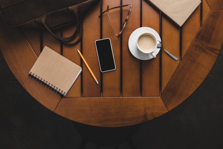 top view of smartphone, notepad and cup of coffee on wooden table
