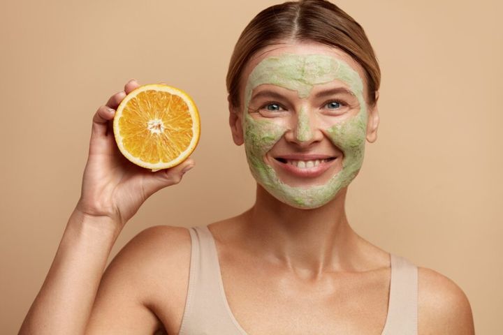 Laughing Face Mask Woman Hold Orange. Positive Woman with Clay Face Mask
