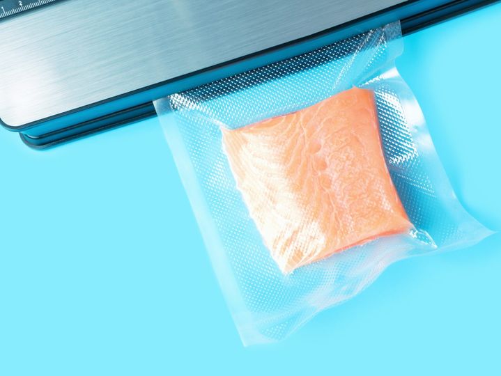 Piece of salmon packed in vacuum bag close up on blue background top view.