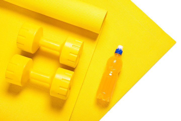 Yellow dumbbells, fitness mat and orange electrolyte drink