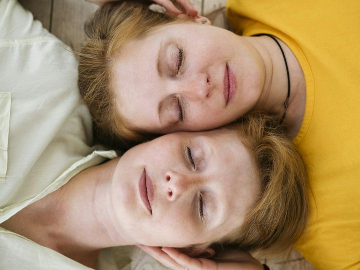 Two red-haired sisters lie cheek to cheek with their eyes closed. Similar women