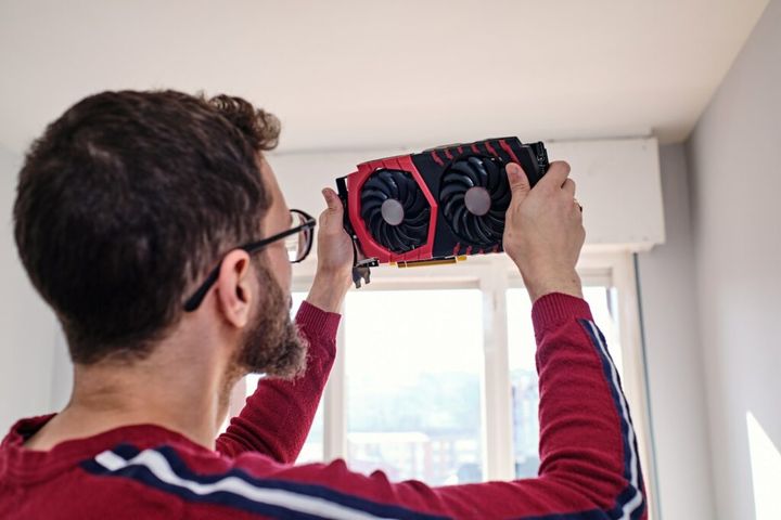 Young man holding and holding up graphic card in his home