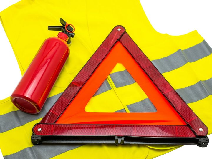 The fire extinguisher and reflective warning triangle lie on the reflective vest, isolated on a whit