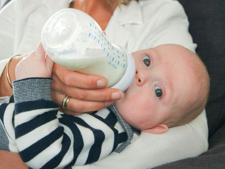 Baby drinks milk from the baby bottle and looking at the camera.