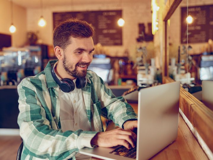 Cheerful bearded man working on laptop in cafeteria