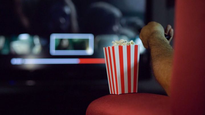 Eating popcorn while watching a movie on the couch at home.