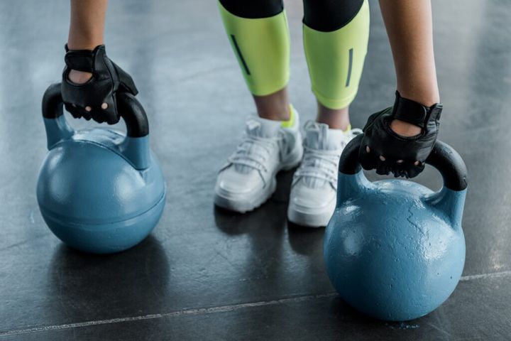 low section of sportswoman in weightlifting gloves training with kettlebells at gym