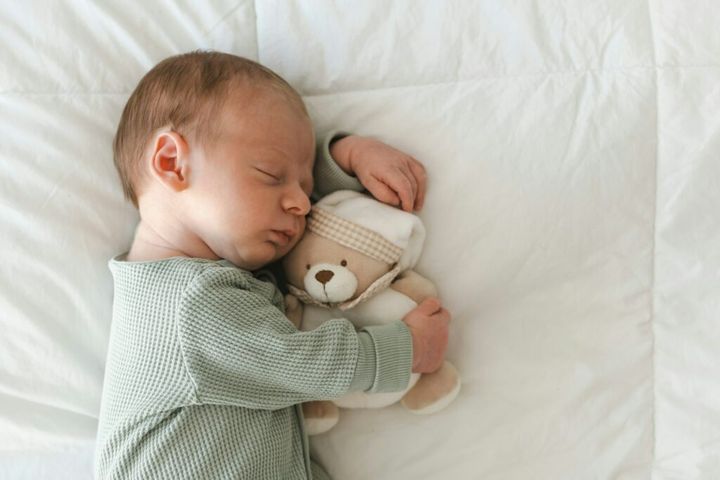 Cute caucasian several days old newborn sleeping on white blanket hugging toy, teddy bear at home